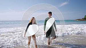 Happy surfers couple in love coming out of ocean waves satisfied with their surf session. Cheerful boy and girl walking