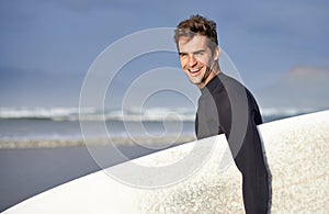 Happy, surfing and portrait of man on beach with surfboard for waves on summer vacation, weekend or holiday by sea