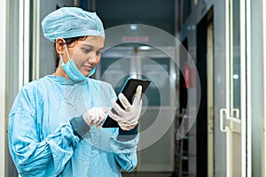 Happy surgeon busy using digital tablet at hospital corridor outside operation theater after surgery - concept of