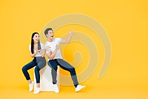 Happy surprised attractive Asian couple pointing and looking at blank space beside in yellow isolated stuidio background