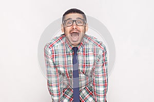 Happy surprised bearded businessman in colorful checkered shirt, blue tie and black eyeglasses standing and looking at camera wit