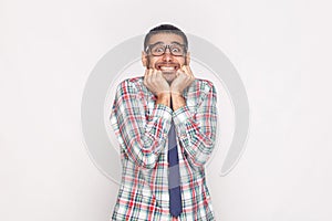 Happy surprised bearded businessman in colorful checkered shirt, blue tie and black eyeglasses standing, touching face and