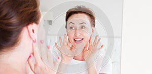 Happy surprised and excited Middle age woman looking in mirror on face. Wrinkles and anti aging skin care concept. Selective focus