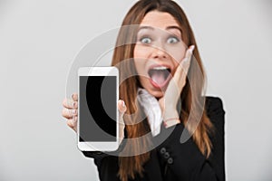 Happy surprised lady showing smartphone with blank screen and looking camera