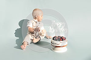 Happy, surprised one year baby boy eats sweets. Toddler boy and first healthy homemade birthday cake with berries on