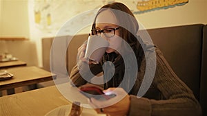 Happy, surprised woman using smartphone sitting in cafe. Young caucasian girl in glasses typing sms and drinking coffee.