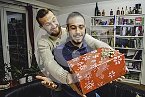 Happy surprised young handsome gay couple celebrating and giving gift at home
