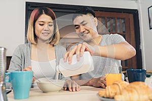 Happy sweet Asian couple having breakfast, cereal in milk, bread and drinking orange juice after wake up in the morning.