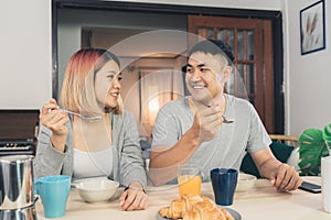 Happy sweet Asian couple having breakfast, cereal in milk, bread and drinking orange juice after wake up in the morning. Husband