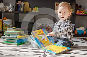 Happy sweet baby boy reading books sitting on the floor, at home