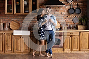 Happy sweet barefooted young couple drinking coffee in kitchen together