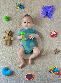 Happy sweet little baby boy on the floor with colorful toys, top view