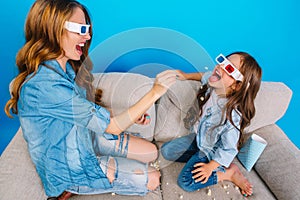 Happy sweet moments beautiful mother with long brunette hair having fun with daughter on couch on blue background