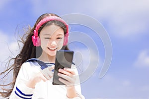 Happy syudent girl  listening music in headphones, holding mobile phone
