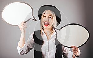 Happy talking. Blonde woman in black hat holding conversation speech bubles on gray background