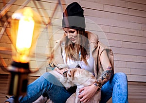Happy tattoed blonde woman playing with her little dogs while sitting on a wooden floor.