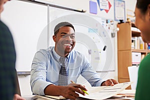 Happy teacher at desk talking to adult education students