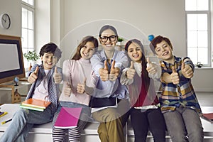 Happy teacher and smiling elementary school students holding thumbs up