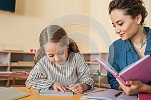 happy teacher smiling near concentrated girl