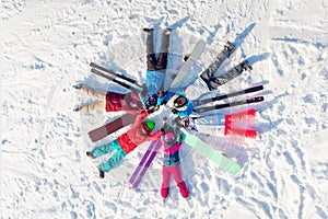 Happy team friends skiers and snowboarders having fun and lying circle on snow with snowboards and ski. Aerial top view