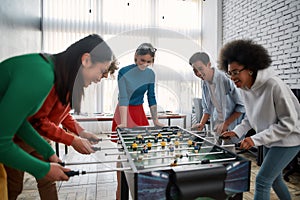 Happy team. Group of young and excited multicultural people in casual wear playing table soccer in the modern office and