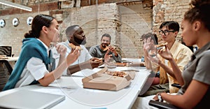 Happy team relaxing at work. Positive multicultural team eating pizza and communicating with each other while having a