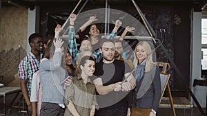 Happy team takes selfie at loft office. Man holds smartphone with self-stick and takes photo of workers, smiling friends