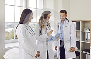 Happy team of young doctors in white uniform standing in hospital or clinic on meeting.