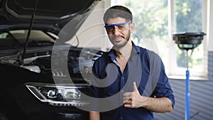 Happy technician bearded brunet mechanic man 20s in safety glasses work in vehicle repair shop show thumb up like