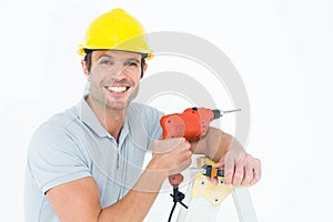 Happy technician holding drill machine while leaning on ladder