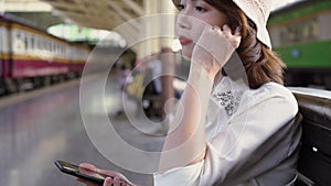 Happy teen Asian woman listening to the music with headphones and waiting in a train station summer. Travel Thailand concept