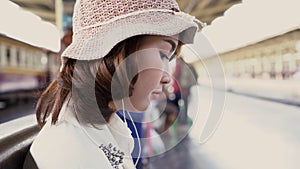 Happy teen Asian woman listening to the music with headphones and waiting in a train station summer. Travel Thailand concept