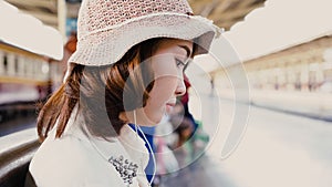 Happy teen Asian woman listening to the music with headphones and waiting in a train station summer. Travel Thailand concept