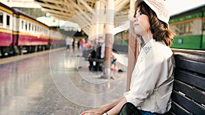 Happy teen Asian woman listening to the music with headphones and waiting in a train station summer. Travel Thailand concept