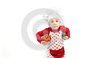 Happy teen boy in chef hat holds pepper and green cucumbers, isolated on white background