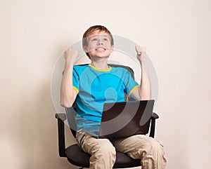 Happy teen boy with laptop in winning pose. Success kid in office chair with portable pc happy ecstatic celebrating being