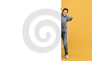Happy Teen Boy Peeking Behind Blank Advertisement Board And Showing Thumb Up