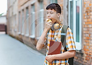 Happy teen boy portrait on the way to school, he is eating an apple, education and back to school concept