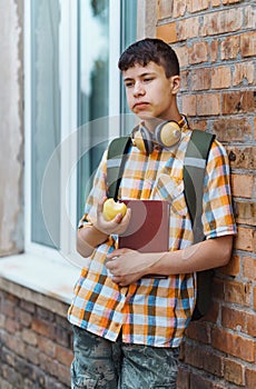 Happy teen boy portrait on the way to school, he is eating an apple, education and back to school concept