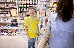 Happy teen boy, school kid carrying a shopping basket smiling looking at camera, buying school stationery in the store