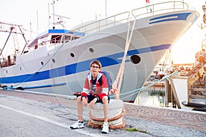 Happy teen boy in sea port dreaming about long journeys against big ship