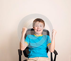 Happy teen boy in winning pose. Success kid in office chair happy ecstatic celebrating being a winner.