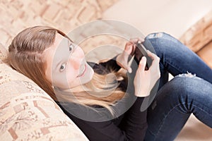 Happy teen with cellphone sitting on the sofa in the living room