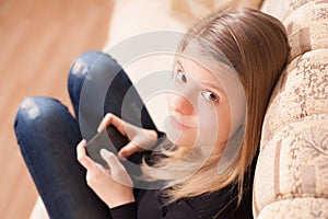 Happy teen with cellphone sitting on the sofa in the living room