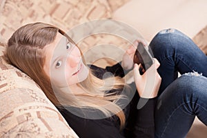 Happy teen with cellphone sitting on the sofa in the living room