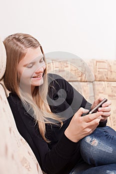 Happy teen with cellphone sitting on the sofa in the living room