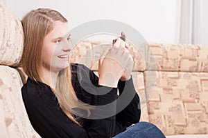 Happy teen with cellphone sitting on the sofa in the living room