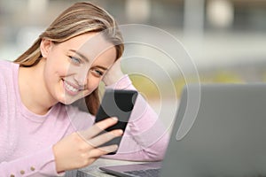 Happy teen checking phone and laptop in the street