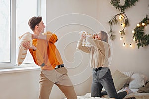 Happy teen couple having fun fighting with pillows on bed in New Years festively decorated bedroom