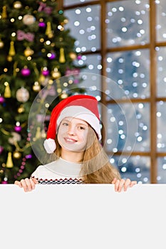 Happy teen girl in christmas hat peeking above white banner